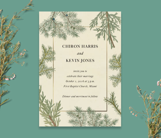 A wedding invitation with a border of evergreen branches propped with sprigs of wildflowers.